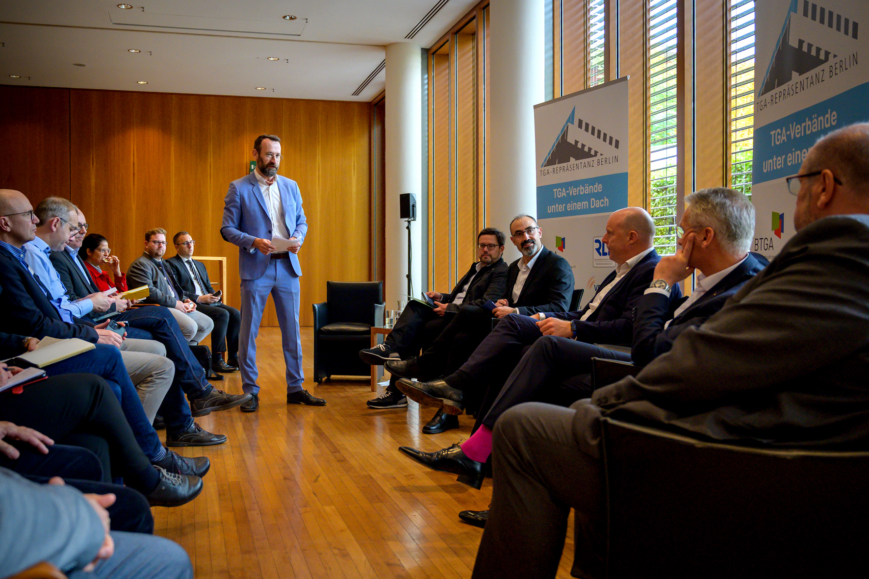 Moderator Jakob Schlandt (stehend) fragt die Bundestagsabgeordneten nach dem aktuellen Stand der Novelle des Gebäudeenergiegesetzes.